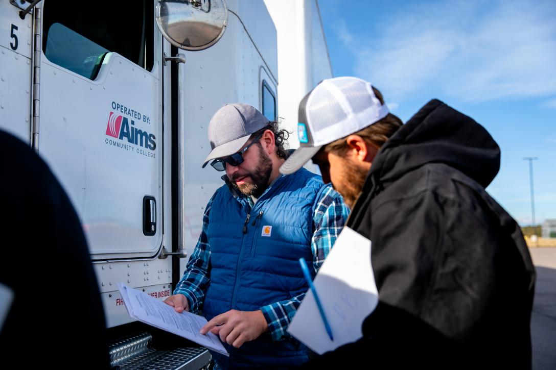 One man with a clipboard talking to another outside of a semi truck