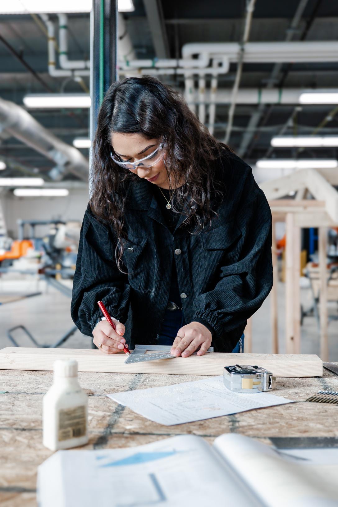 Female student in construction shop measuring wood