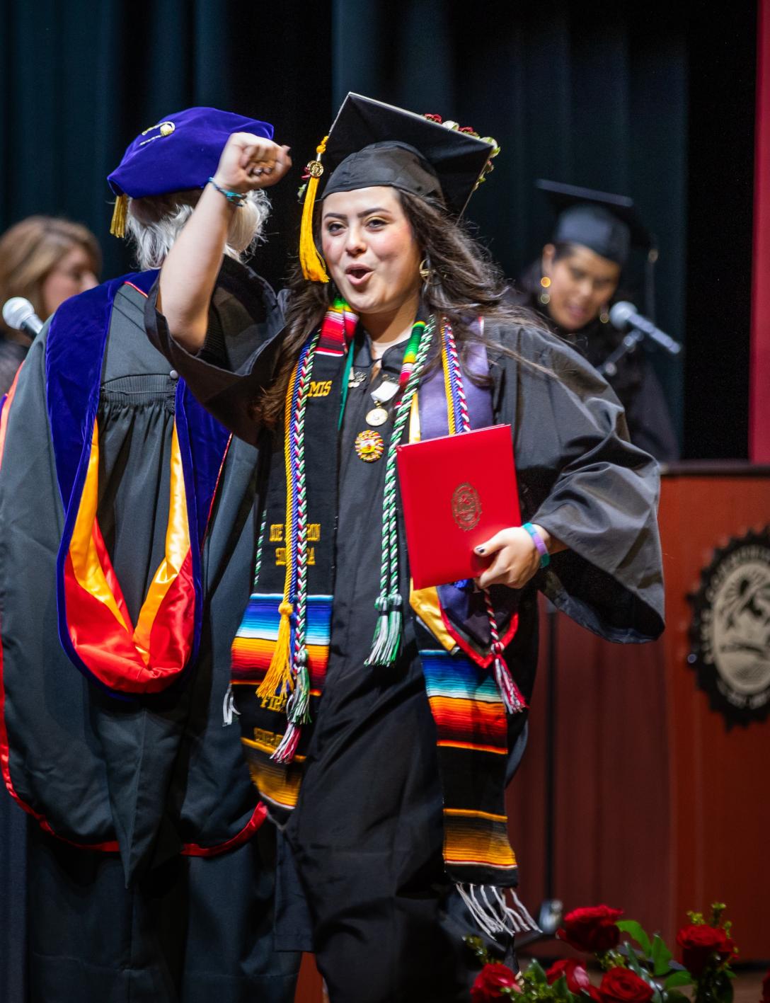 A graduate fist-pumping during commencement while wearing cap and gown and regalia